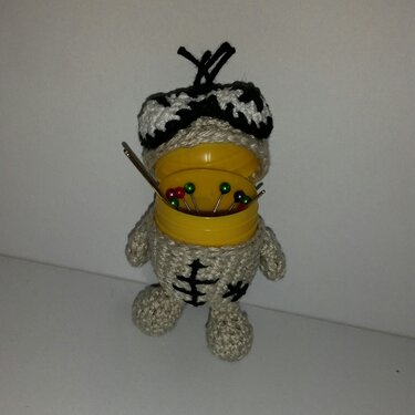 Beige gehäkeltes Skelett‑Amigurumi mit schwarzer Stickerei und geöffneter gelber Dose voller Stecknadeln