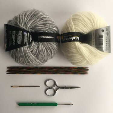 Grau- und cremefarbenes Garn mit Nadelspiel, Schere, Stopfnadel und Häkelnadel, Draufsicht