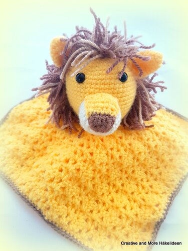 Gelbes gehäkeltes Löwen-Schmusetuch mit brauner Mähne und schwarzen Augen auf hellem Hintergrund