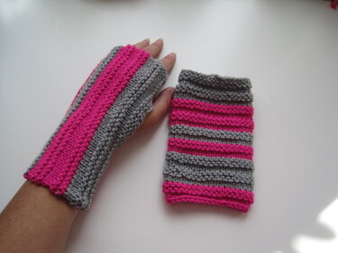 Paar gestrickter fingerloser Armstulpen in Grau und Pink; eine an einer Hand getragen, eine daneben liegend