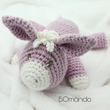 Gehäkeltes lila Amigurumi‑Eselchen mit weißen Details auf weißem Stoff