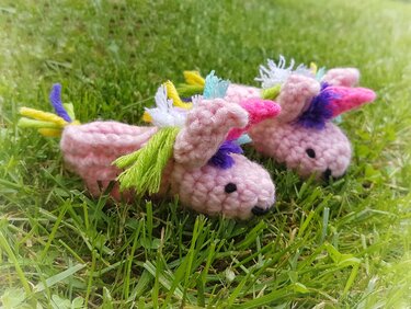 Zwei rosa gehäkelte Einhorn-Babyschuhe mit bunten Mähnen im Gras.