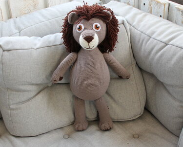 Gehäkelter Amigurumi-Löwe mit brauner Mähne sitzt auf hellem Sofa