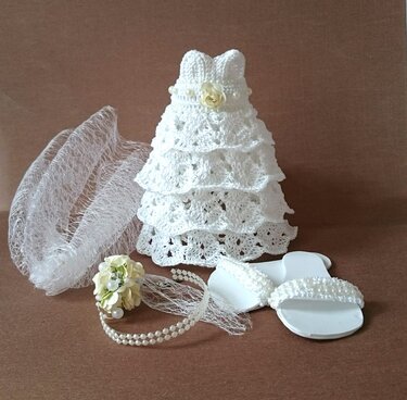 Gehäkeltes Puppen-Brautset mit Kleid, Schleier, Haarreif und Sandalen auf braunem Hintergrund