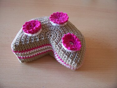 Gehäkeltes herzförmiges Stück Kuchen in beige mit weißen und pinken Streifen und drei pinken Häkelrosen