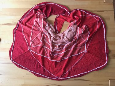 Halbmondförmiges gestricktes Tuch in Rot- und Pinktönen mit weißen Maschenreihen auf Holzuntergrund