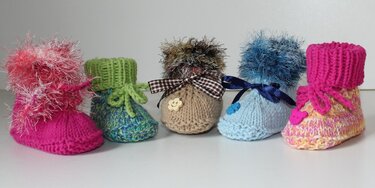 Reihe von fünf gestrickten Babyschuhen in unterschiedlichen Farben und Mustern, verziert mit Schleifen und Knöpfen