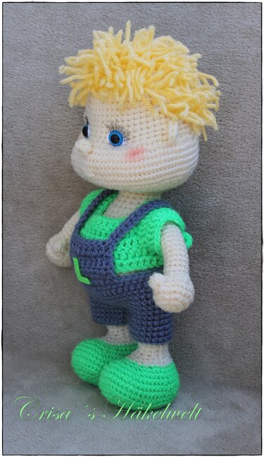 Handgehäkelte Amigurumi-Jungenpuppe mit gelbem Garnhaar, blauer Latzhose und grünen Schuhen