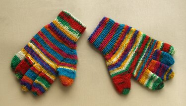 Zwei gestrickte Kinderhandschuhe mit bunten Querstreifen auf hellem Hintergrund.