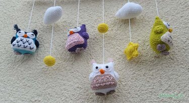 Vier gehäkelte Amigurumi-Eulen in verschiedenen Farben als Mobile mit Wolken, gelben Kugeln und Stern vor heller Wand
