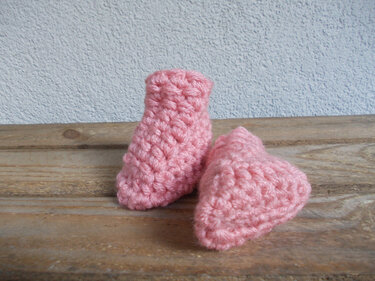 paar rosa Baby-Booties aus grober Masche auf Holzbrett