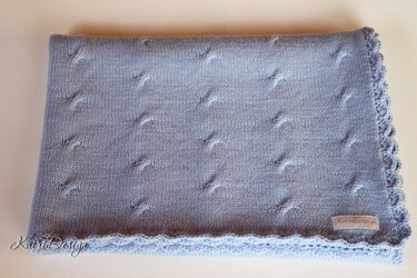 Folded light blue machine-knitted blanket showing raised stitch motifs and scalloped edge.