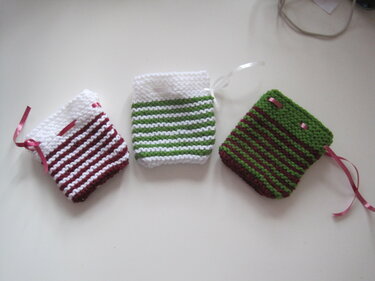 Drei gestrickte, gestreifte Weihnachtssäckchen mit Satinbändern in Rot, Grün und Weiß