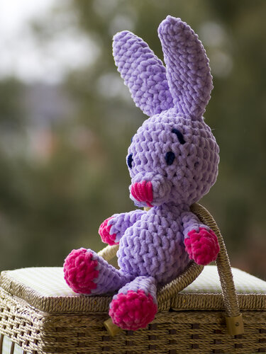 Gehäkelter violetter Amigurumi-Hase mit pinken Pfoten auf Korb