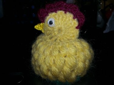Handgehäkeltes gelbes Küken mit dunkelrotem Kamm und Wackelaugen, als Eierwärmer geeignet.