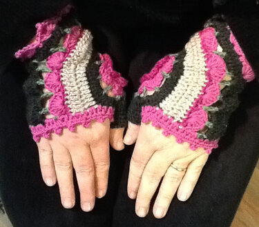 Nahaufnahme von Händen mit gehäkelten, fingerlosen Handschuhen in Pink, Schwarz und Beige.