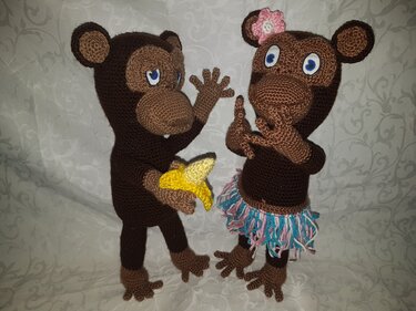 Zwei gehäkelte Amigurumi-Affen, einer mit Banane, einer mit Fransenrock und Blüte