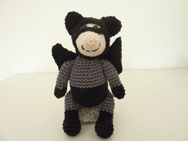 Vorderansicht eines gehäkelten Amigurumi mit Maske und Flügeln in Grau-Schwarz