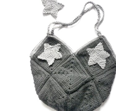 Gehäkelte Henkeltasche aus dunklen Granny Squares mit hellgrauen Stern-Applikationen und gedrehtem Träger