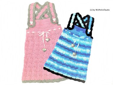 Zwei gehäkelte Kinderkleider: rosa mit grauen, gekreuzten Trägern und Herzknöpfen; blau gestreift mit schwarzen Trägern und Herzanhängern.