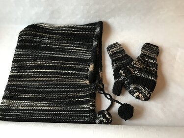 Schwarz-weiß gestreifter Schal mit Bommelbändern neben einem Paar gestrickter Fäustlinge auf hellem Untergrund