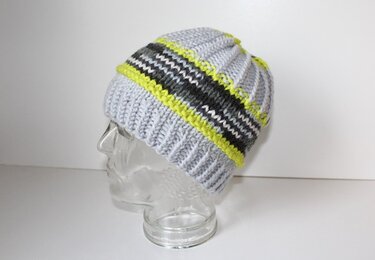 Gestrickte Mütze in Hellgrau mit Streifen in Neongelb, Dunkelgrau und Weiß auf einem transparenten Kopfmodell.