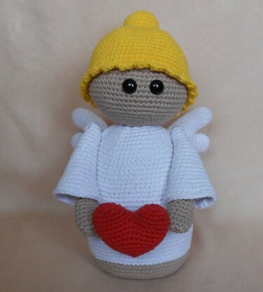 Gehäkelter Amigurumi-Engel mit gelber Mütze hält rotes Herz