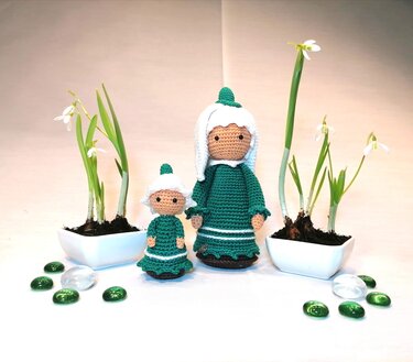 Große und kleine gehäkelte Amigurumi-Puppen in grünen Kleidern neben Schneeglöckchen