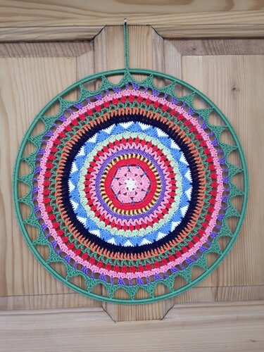 Gehäkeltes buntes Mandala mit konzentrischen Mustern in grünem Ring an Holztür