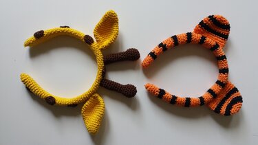 Zwei gehäkelte Haarreifen: gelbe Giraffe und orange-schwarz gestreifter Tiger auf weißem Hintergrund.