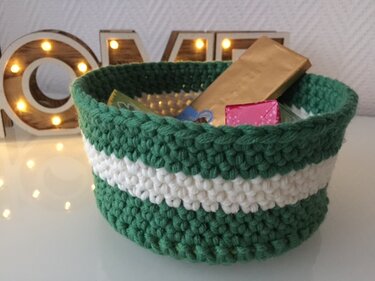 Handgehäkelter Korb in Dunkelgrün mit weißem Streifen, gefüllt mit kleinen Geschenken