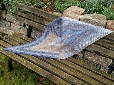 Gestricktes Dreieckstuch in Blau-, Beige- und Grautönen auf rustikaler Holzbank