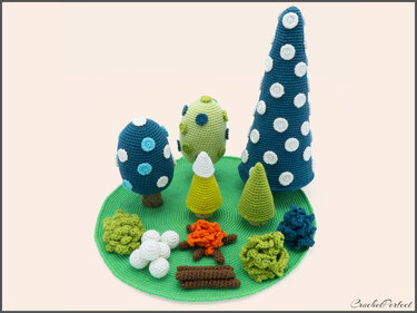 Gehäkeltes Amigurumi-Waldspielset auf rundem grünen Untergrund mit Bäumen, Büschen, Lagerfeuer und weißen Dekokugeln