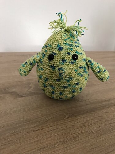 Birnenförmiges gehäkeltes Amigurumi in grün-blau mit schwarzen Sicherheitsaugen und Fransen oben
