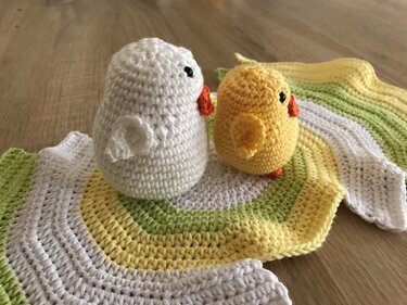 Zwei gehäkelte Küken (weiß und gelb) auf rund gestreifter Häkeldecke in Weiß, Gelb und Grün.