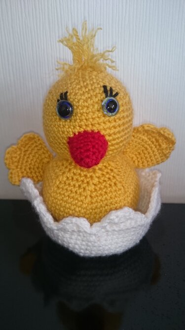 Gehäkeltes gelbes Amigurumi-Küken mit rotem Schnabel in weißer gezackter Eierschale