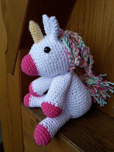 Seitenansicht eines gehäkelten Einhorn-Amigurumi mit rosa Hufen und mehrfarbiger Mähne