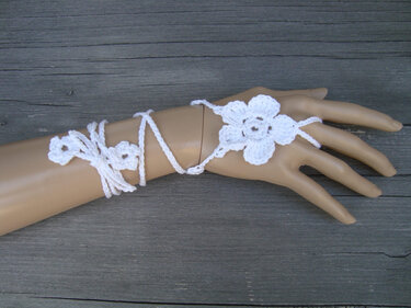 Weiße gehäkelte Blüten als Boho-Handschmuck auf einer Modellhand mit gewickelten Kordeln