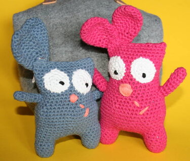 Zwei gehäkelte Amigurumi-Hasen, einer blau, einer pink, mit großen weißen Augen