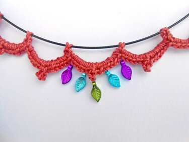 Filigrane korallrote Häkelborte mit bunten metallisch schimmernden Blatt-Anhängern an schwarzer Kordel, Detailaufnahme