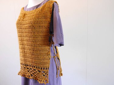 Senfgelbes gehäkeltes Damen-Top mit Rundhalsausschnitt, Lochmuster am Saum und seitlichen Bindebändern auf einem Mannequin.