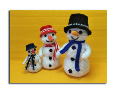Drei Amigurumi‑Schneemänner unterschiedlicher Größe mit Hut und Schal