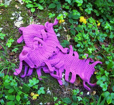 Lila gehäkelter Schal mit Schlaufen auf moosigem Waldboden