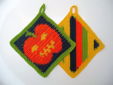 Zwei gehäkelte Topflappen, einer mit Kürbismotiv, der andere gestreift.