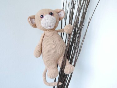 Nahaufnahme eines beigen gehäkelten Amigurumi-Äffchens mit erkennbaren Kopf-, Körper- und Gliedmaßenformen