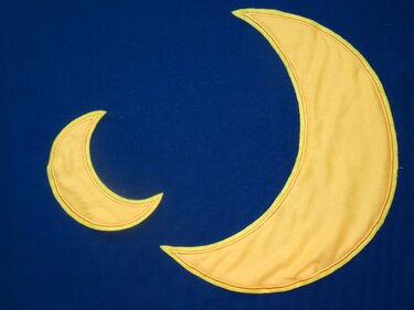 Zwei gelbe Sichelmonde (groß und klein) auf dunkelblauem Stoff gestickt.