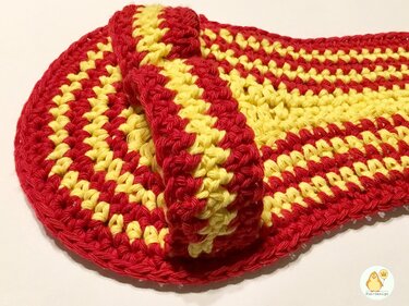 Nahaufnahme eines gehäkelten Pantoffels mit roten und gelben Streifen auf hellem Hintergrund.