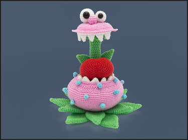 Gehäkelte rosa‑grüne Monsterpflanze mit großen Augen, weißen Zähnen und rotem Einsatz auf dunkelblauem Hintergrund.