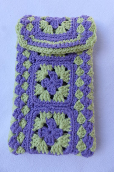 Gehäkeltes Utensilo aus Granny Squares in Lila und Hellgrün mit Überschlagklappe auf hellem Hintergrund