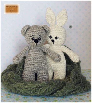 Gehäkelter grauer Teddybär und weißer Hase in grünem Wollnest